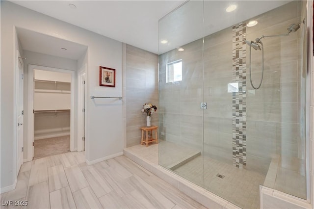 bathroom featuring a walk in shower, a spacious closet, and baseboards