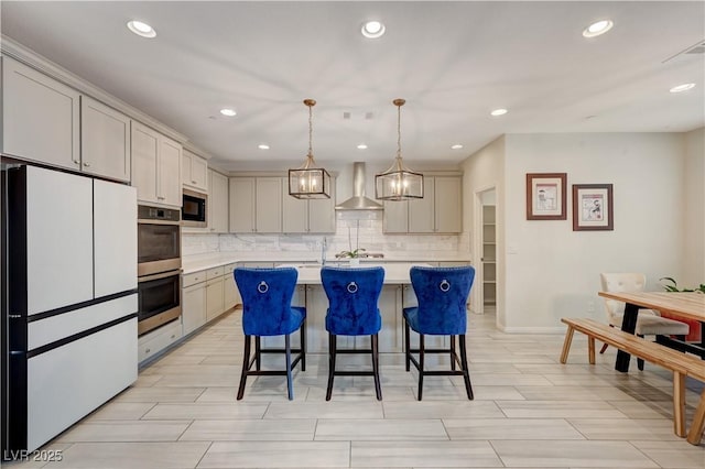 kitchen with wall chimney range hood, a center island with sink, light countertops, and freestanding refrigerator