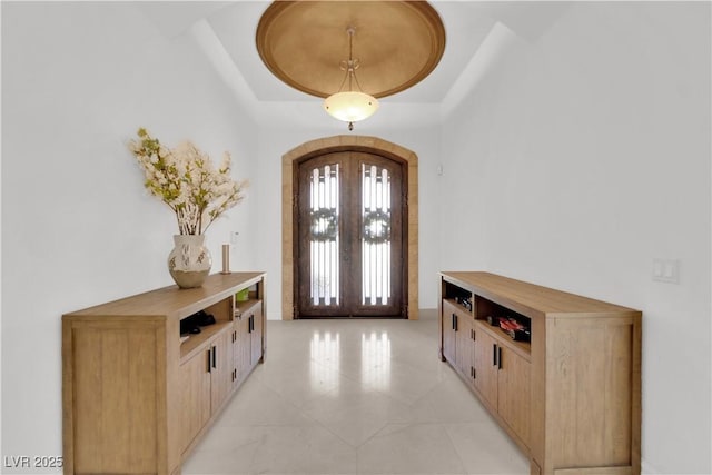 entryway featuring arched walkways, a raised ceiling, and french doors