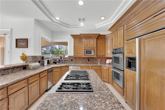 kitchen featuring visible vents, a raised ceiling, built in appliances, light stone countertops, and a sink