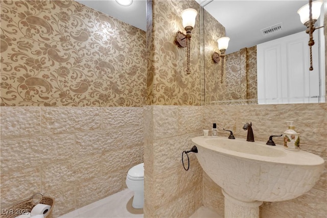 bathroom with tile patterned flooring, toilet, a sink, visible vents, and tile walls