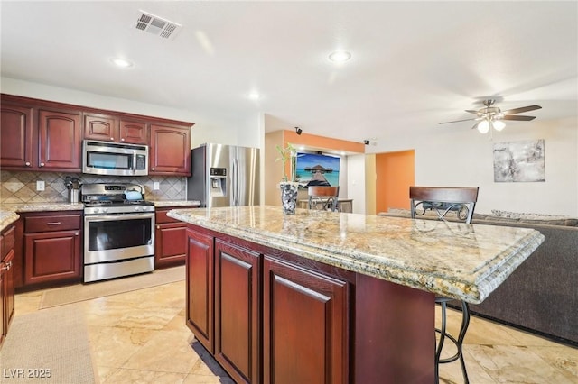 kitchen with a breakfast bar area, stainless steel appliances, a center island, visible vents, and decorative backsplash