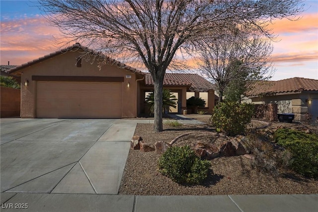 view of front of house with a garage, driveway, a tiled roof, and stucco siding