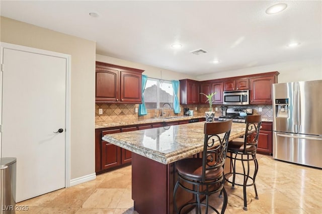 kitchen featuring light stone counters, a sink, visible vents, appliances with stainless steel finishes, and a center island