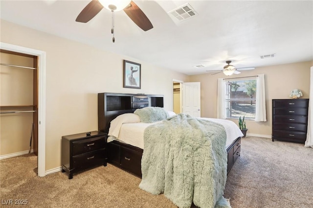 bedroom with a walk in closet, visible vents, light carpet, and baseboards