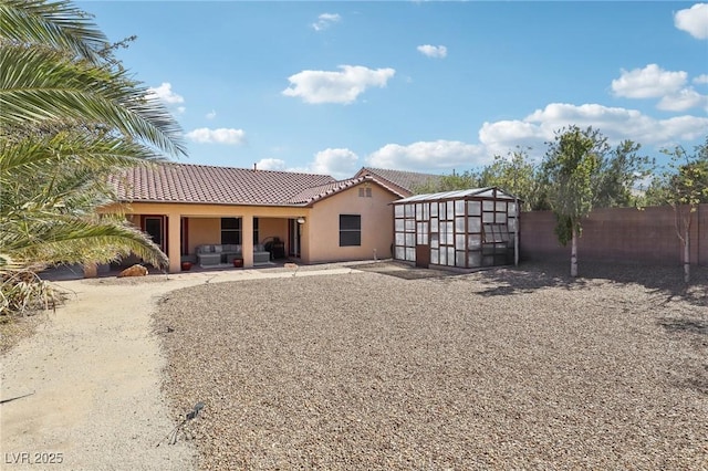 rear view of house featuring a tiled roof, fence, and stucco siding