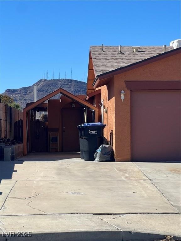 view of side of property featuring a shingled roof, concrete driveway, fence, a mountain view, and stucco siding