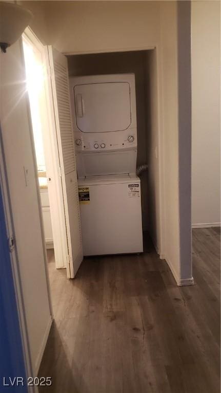 clothes washing area featuring stacked washer and dryer, baseboards, laundry area, and dark wood-style flooring