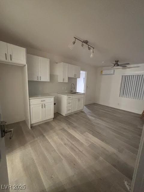 kitchen with light wood-type flooring, white cabinets, a wall unit AC, and a sink