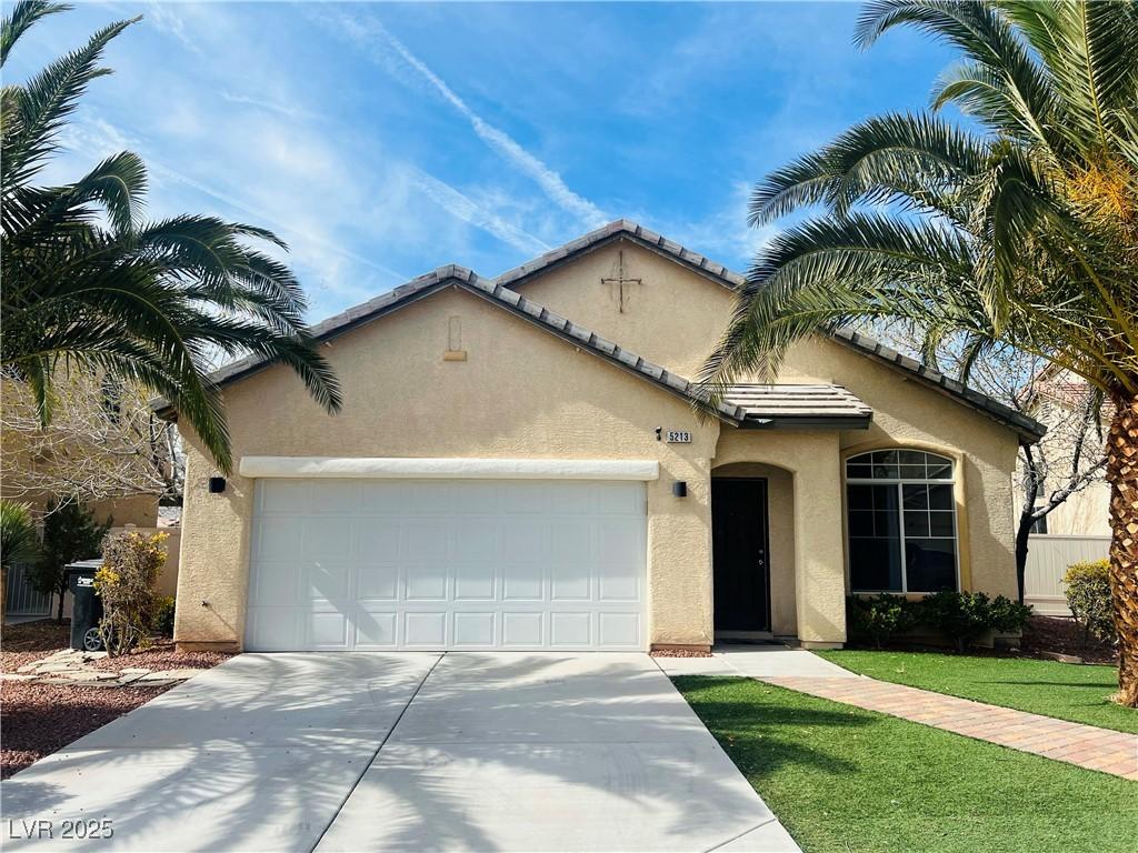 mediterranean / spanish home with a garage, concrete driveway, a front lawn, and stucco siding