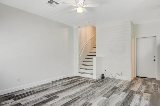 spare room featuring ceiling fan, wood finished floors, visible vents, baseboards, and stairs