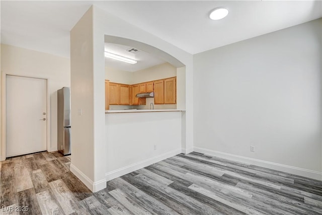 kitchen featuring baseboards, arched walkways, wood finished floors, freestanding refrigerator, and under cabinet range hood