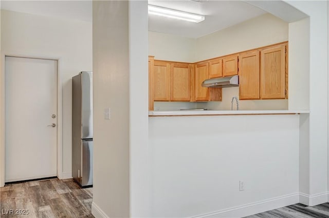 kitchen with light countertops, wood finished floors, freestanding refrigerator, and under cabinet range hood