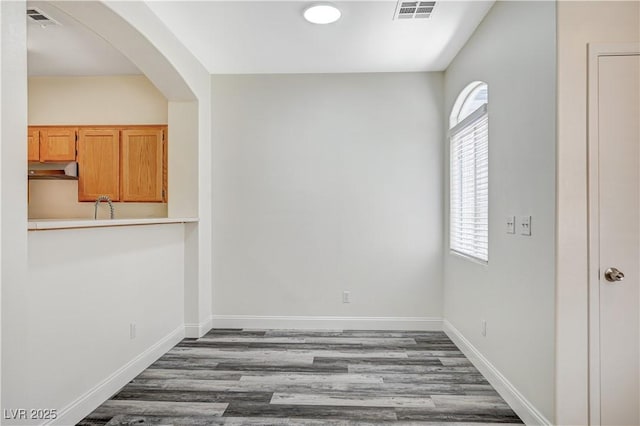 empty room featuring baseboards, visible vents, arched walkways, and wood finished floors