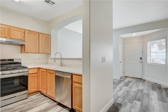 kitchen featuring light wood-style floors, appliances with stainless steel finishes, light countertops, under cabinet range hood, and a sink