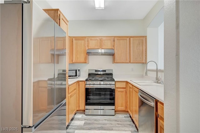 kitchen with light countertops, light brown cabinetry, appliances with stainless steel finishes, a sink, and under cabinet range hood