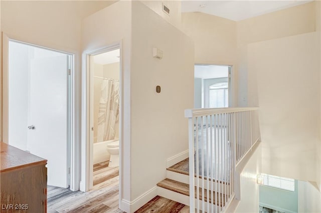 stairs featuring baseboards, visible vents, vaulted ceiling, and wood finished floors