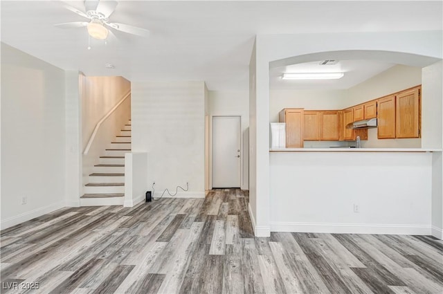 kitchen featuring arched walkways, light wood-style flooring, under cabinet range hood, visible vents, and baseboards