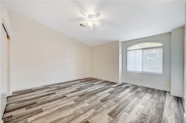 spare room with ceiling fan, visible vents, baseboards, and wood finished floors