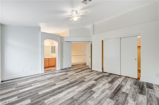 unfurnished bedroom featuring light wood-type flooring, visible vents, arched walkways, and a closet