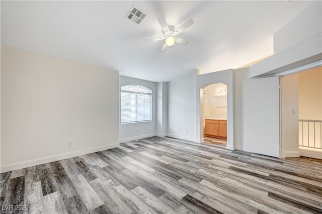 empty room with arched walkways, ceiling fan, light wood-style flooring, visible vents, and baseboards