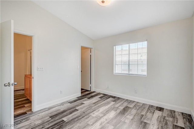 unfurnished bedroom with light wood-style floors, baseboards, and vaulted ceiling