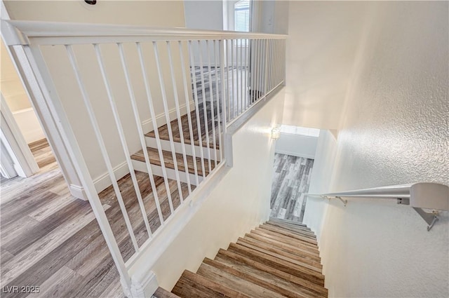 staircase with a textured wall, baseboards, and wood finished floors