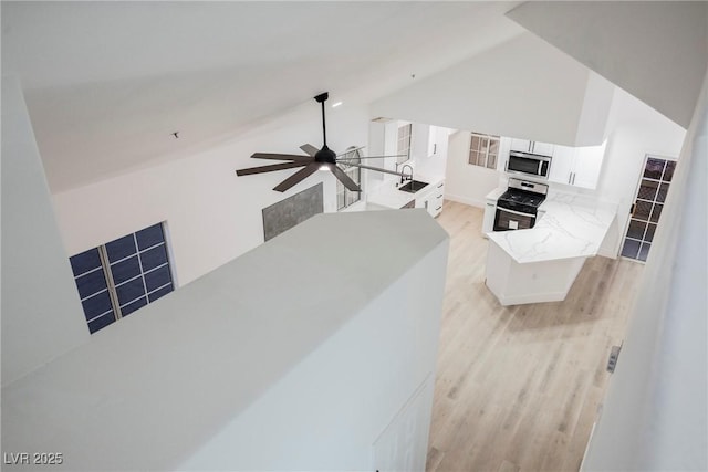 kitchen with white cabinets, appliances with stainless steel finishes, a peninsula, light wood-style floors, and a sink