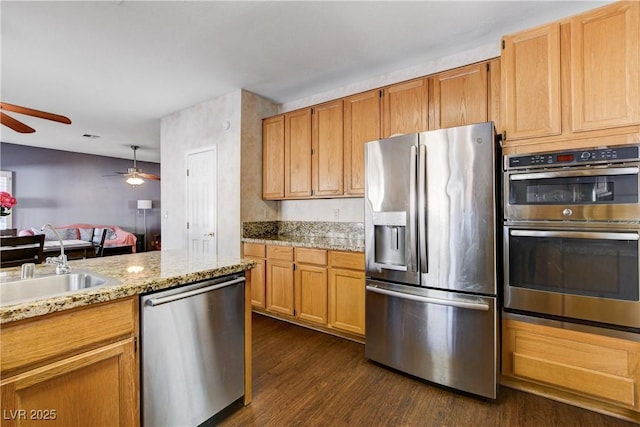 kitchen featuring light stone counters, a sink, a ceiling fan, appliances with stainless steel finishes, and dark wood-style floors