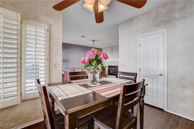 dining space with ceiling fan, a fireplace, baseboards, and dark wood-style flooring