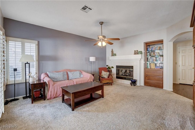 living area with carpet floors, arched walkways, visible vents, ceiling fan, and a tile fireplace