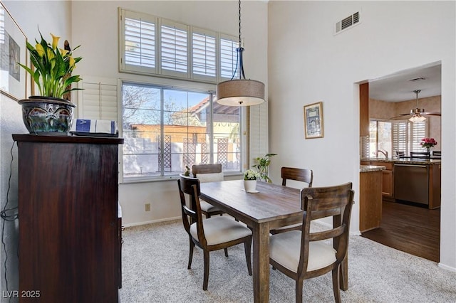 dining area with baseboards, light colored carpet, visible vents, and a high ceiling