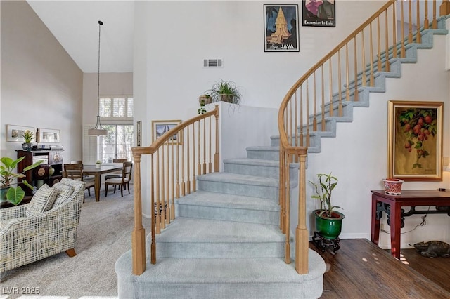 staircase with visible vents, wood finished floors, a towering ceiling, and baseboards