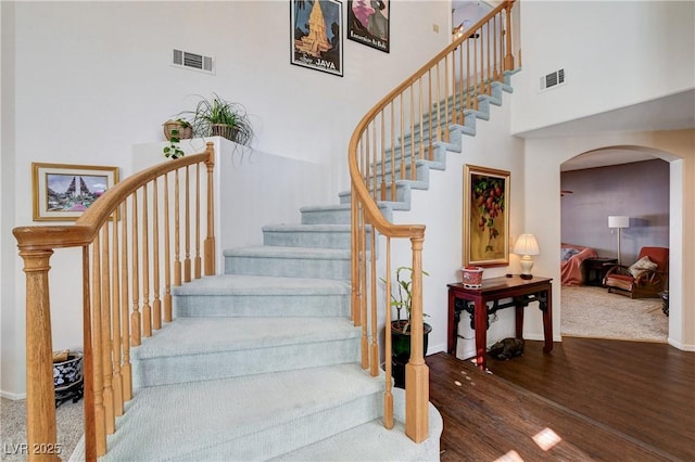 staircase with a towering ceiling, visible vents, arched walkways, and wood finished floors