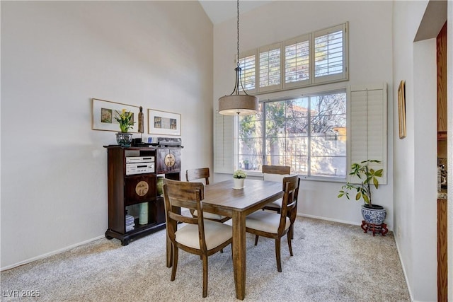 dining room with light carpet, a towering ceiling, and baseboards