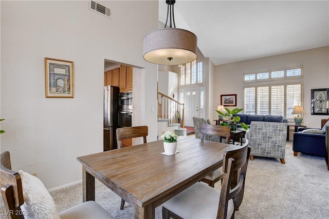 dining space with visible vents, plenty of natural light, light carpet, and a high ceiling