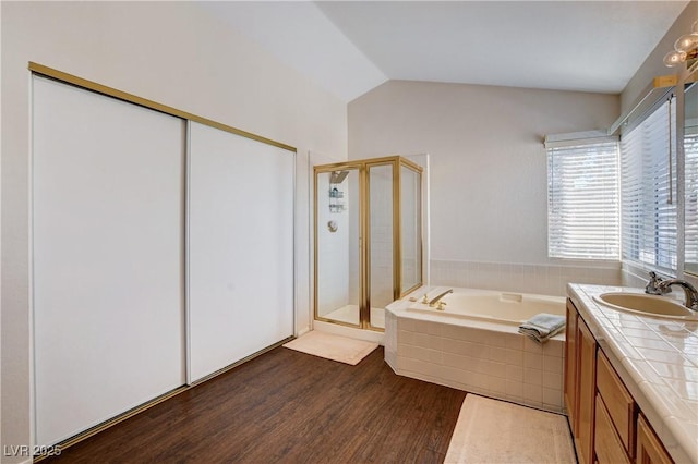 bathroom featuring lofted ceiling, wood finished floors, vanity, a bath, and a stall shower