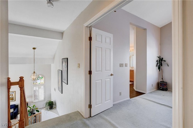 hall featuring lofted ceiling, baseboards, carpet floors, and a notable chandelier