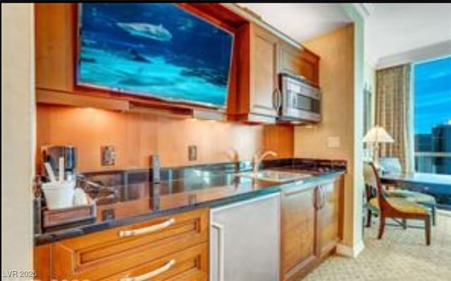 kitchen featuring stainless steel microwave, dark countertops, a sink, and brown cabinetry