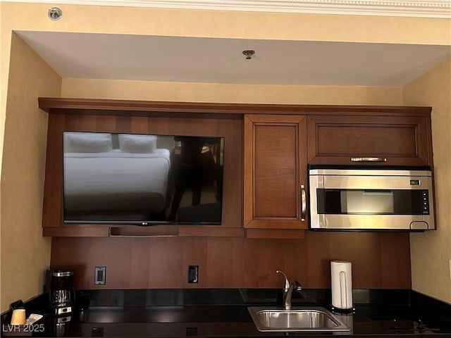 kitchen with stainless steel microwave, dark countertops, a sink, and brown cabinetry