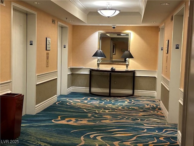 hallway with a decorative wall, a wainscoted wall, crown molding, a tray ceiling, and elevator