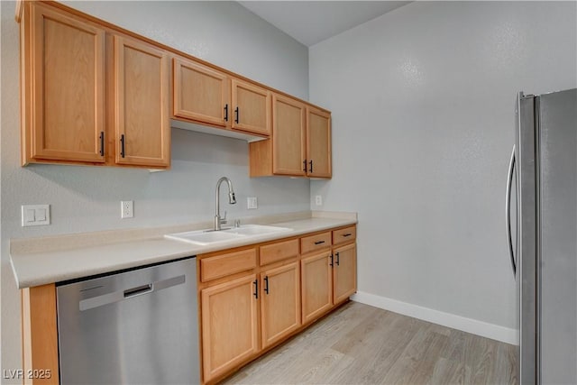 kitchen featuring stainless steel appliances, light countertops, light wood-style flooring, a sink, and baseboards