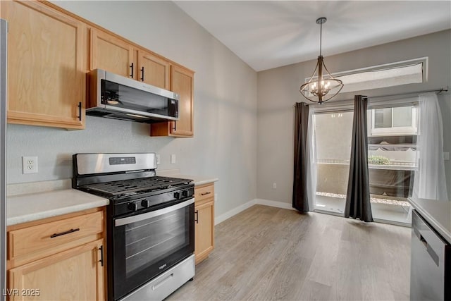 kitchen featuring appliances with stainless steel finishes, light countertops, light brown cabinetry, a chandelier, and pendant lighting