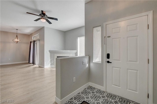 entryway with ceiling fan, light wood-type flooring, a fireplace, and baseboards