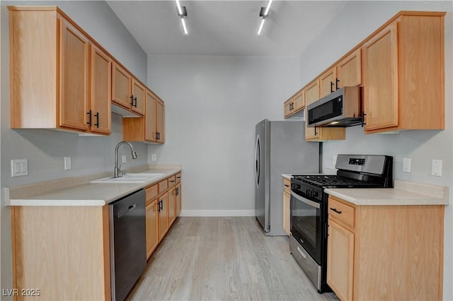 kitchen featuring appliances with stainless steel finishes, light countertops, light wood-style floors, light brown cabinets, and a sink