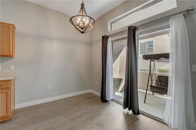 unfurnished dining area with a chandelier, light wood-style flooring, and baseboards