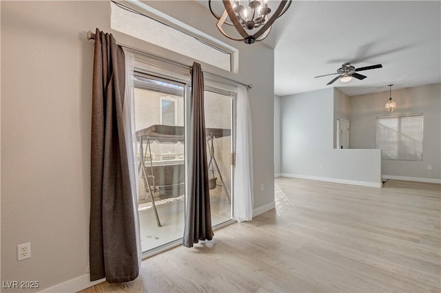 spare room featuring ceiling fan with notable chandelier, light wood-type flooring, and baseboards