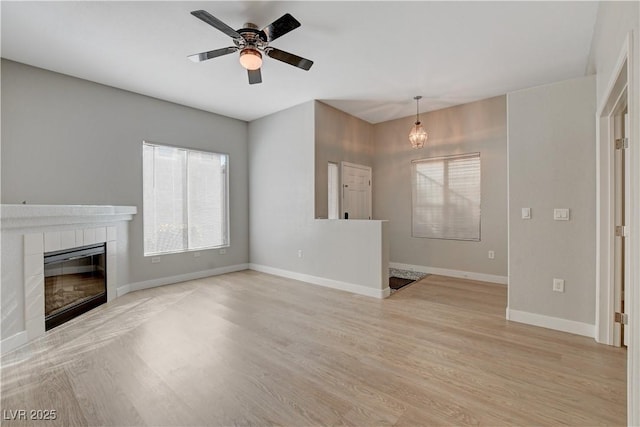 unfurnished living room featuring light wood-style floors, a tile fireplace, baseboards, and a ceiling fan