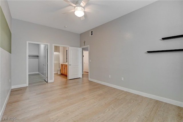 unfurnished bedroom featuring light wood-style flooring, a spacious closet, baseboards, and ceiling fan