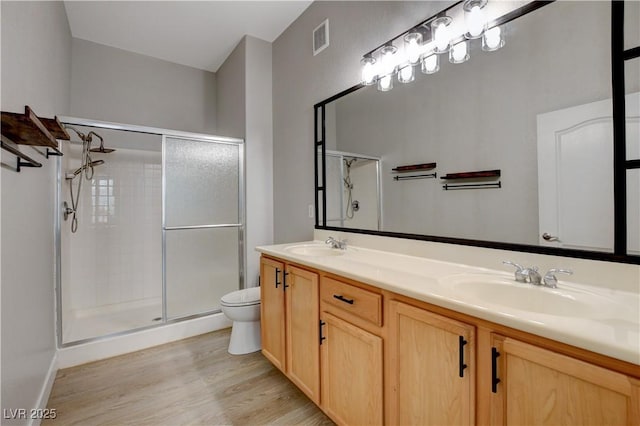 bathroom with double vanity, a stall shower, toilet, wood finished floors, and a sink